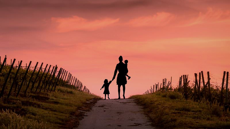 Mutter läuft mit ihren beiden Kindern dem Sonnenuntergang entgegen.