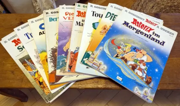 Foto mehrerer Asterix-Comics von René Goscinny und Albert Uderzo, fächerförmig auf einem Holztisch ausgebreitet, im Vordergrund „Asterix im Morgenland“.