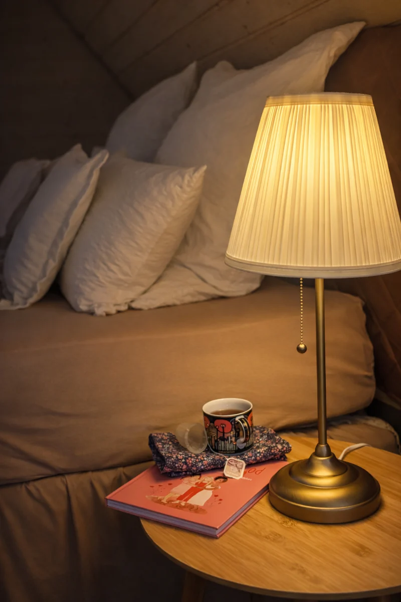 Buch, Tasse Tee und Menstruationsprodukte liegen auf einem Nachttisch neben einem Bett.