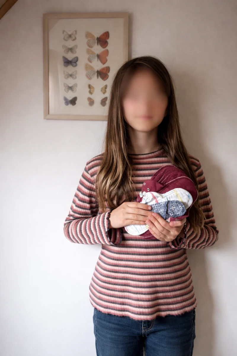 Teenager hält mehrere waschbare Stoffbinden als nachhaltige Menstruationsprodukte in den Händen.