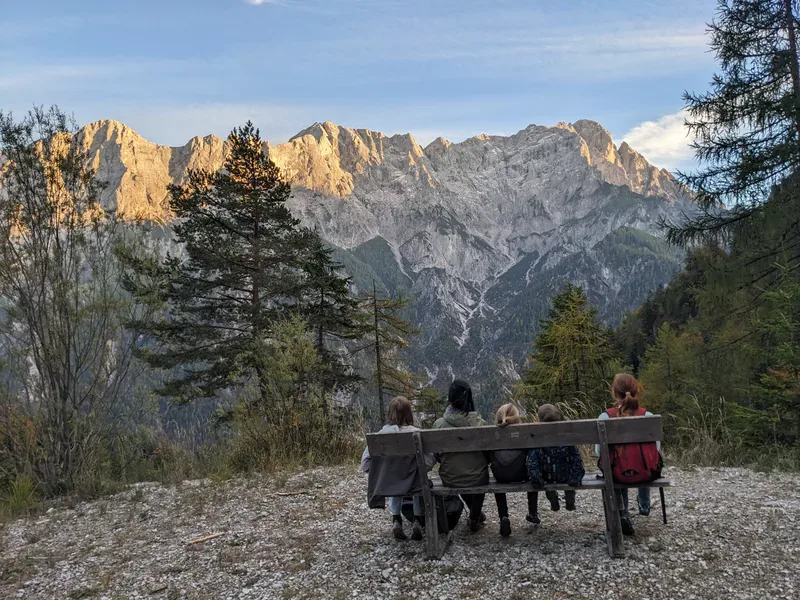Vier Kinder und eine erwachsene Person sitzen auf einer Bank vor einer Bergkulisse.