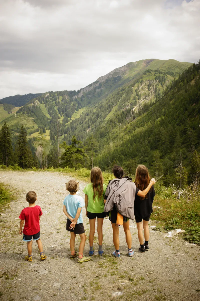Fünf Kinder stehen mit dem Rücken zur Kamera vor einer Berglandschaft.