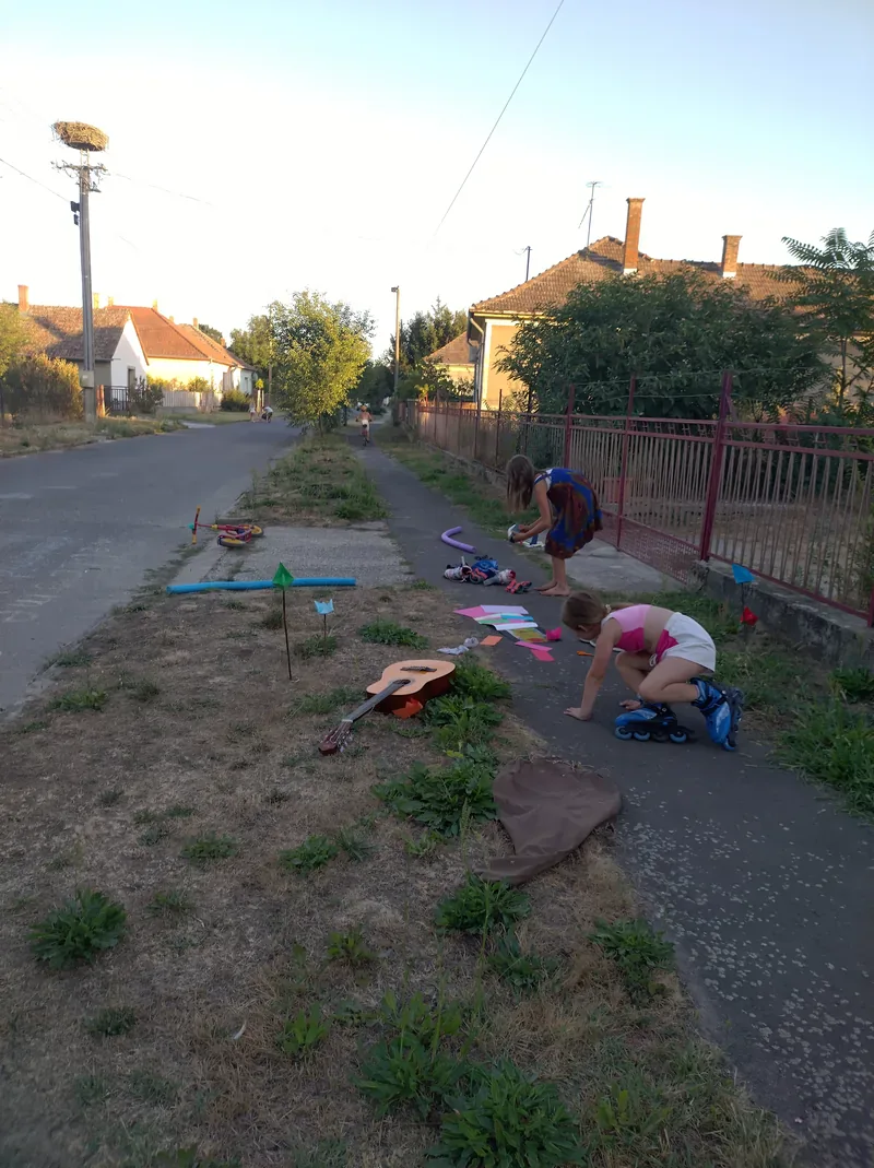 Zwei Kinder spielen auf einem Gehweg mit Bastelsachen, Rollschuhen und einer Gitarre.
